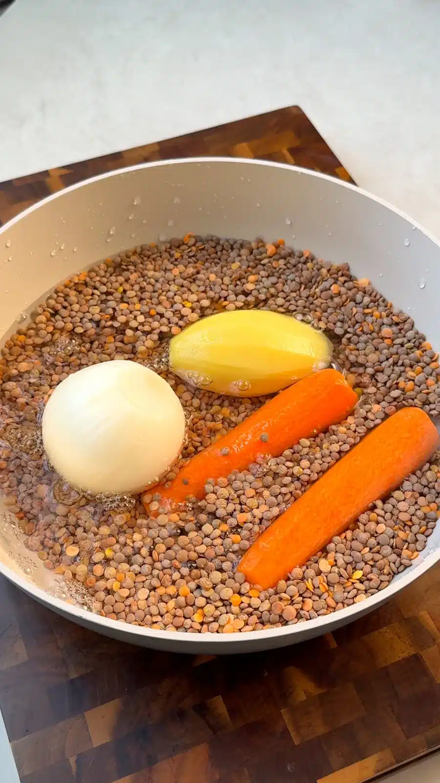 Dry lentils with a peeled onion, potato and carrots in water
