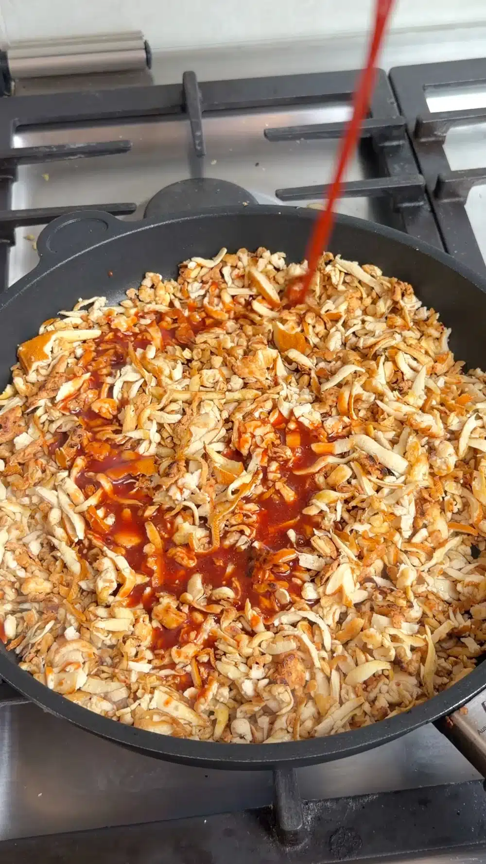 Tomato and soy glaze being poured over browned grated tofu