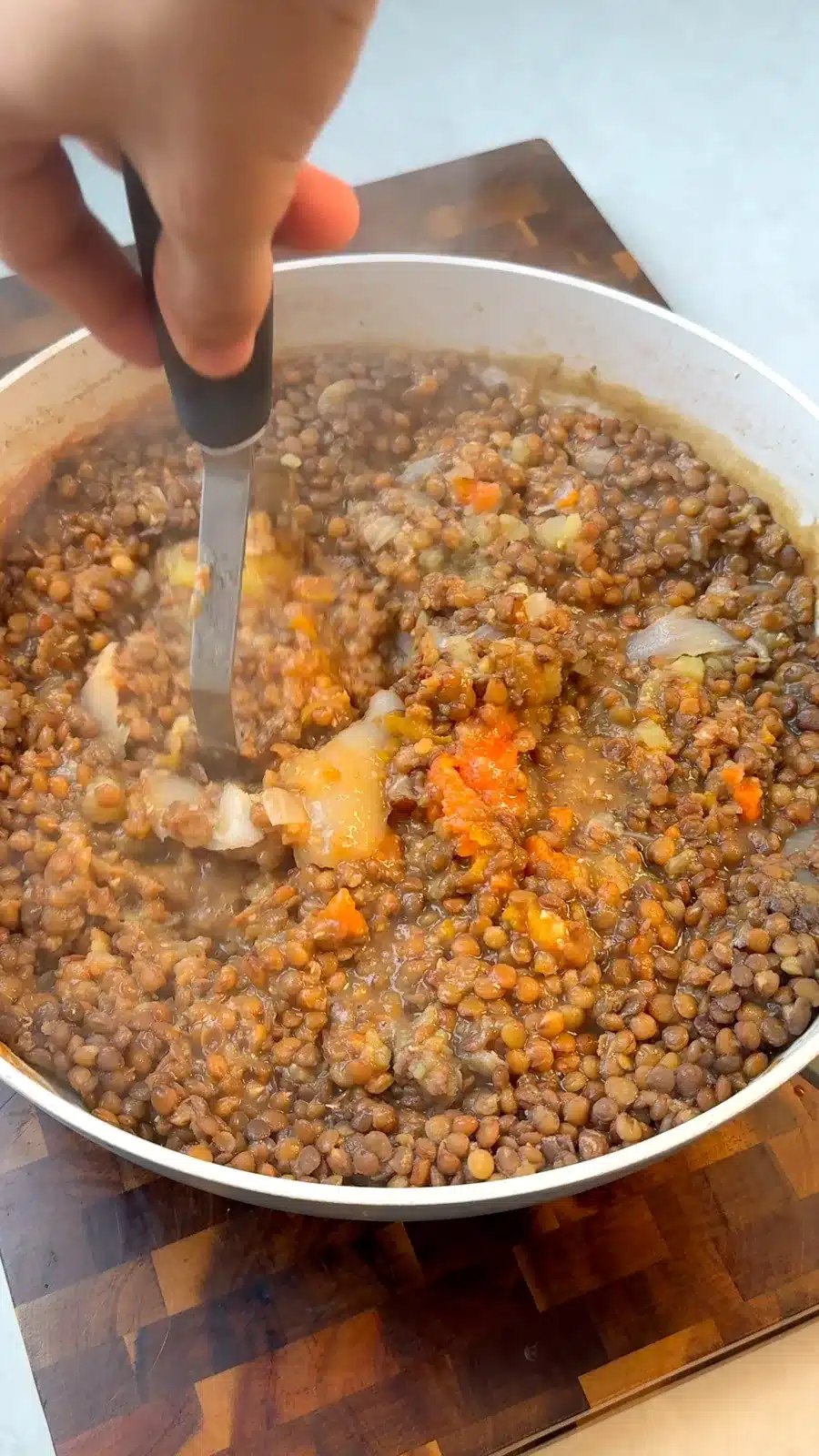 Cooked lentils and vegetables being mashed by hand