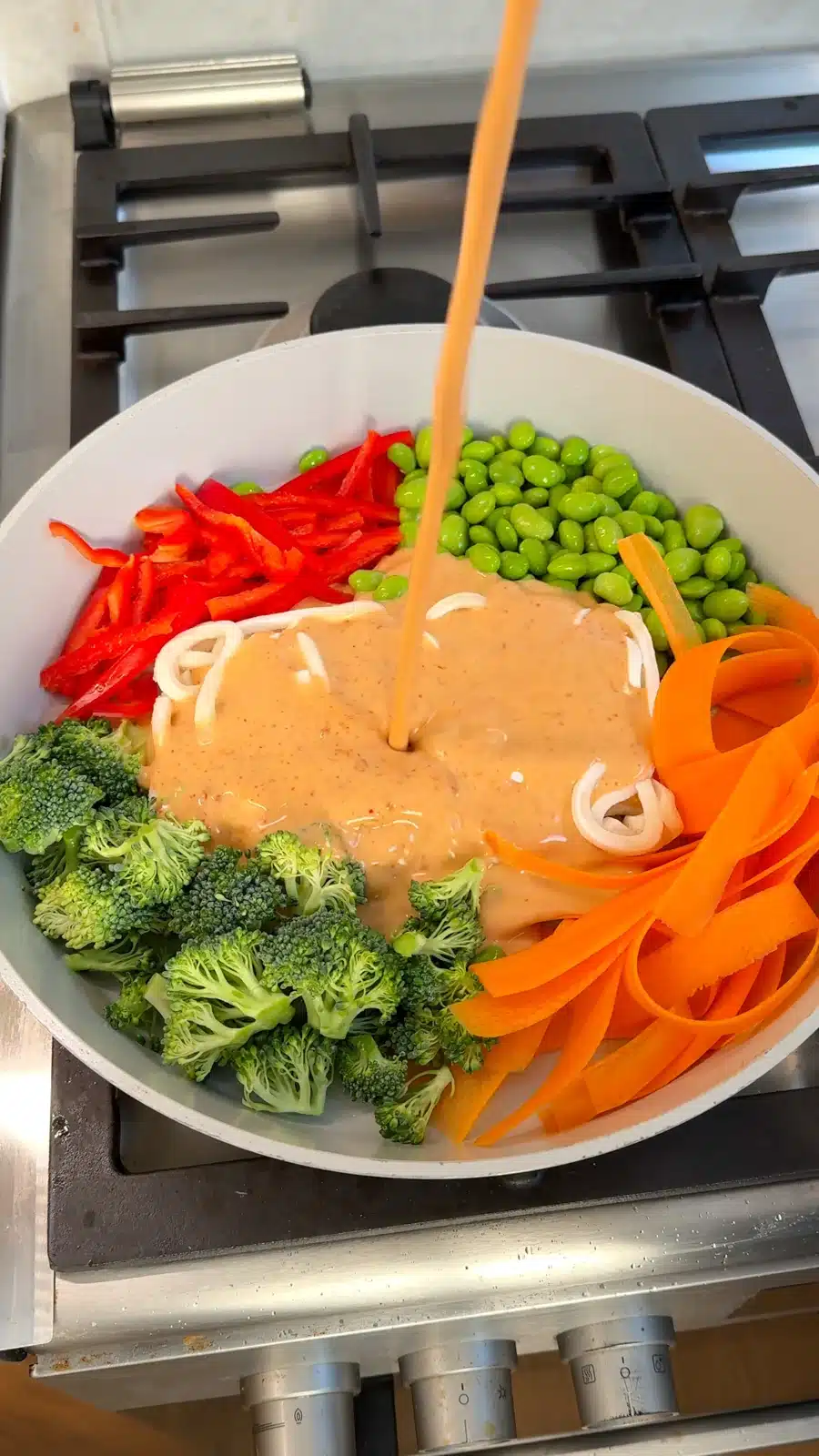 Coconut milk and peanut curry sauce being poured over udon and vegetables
