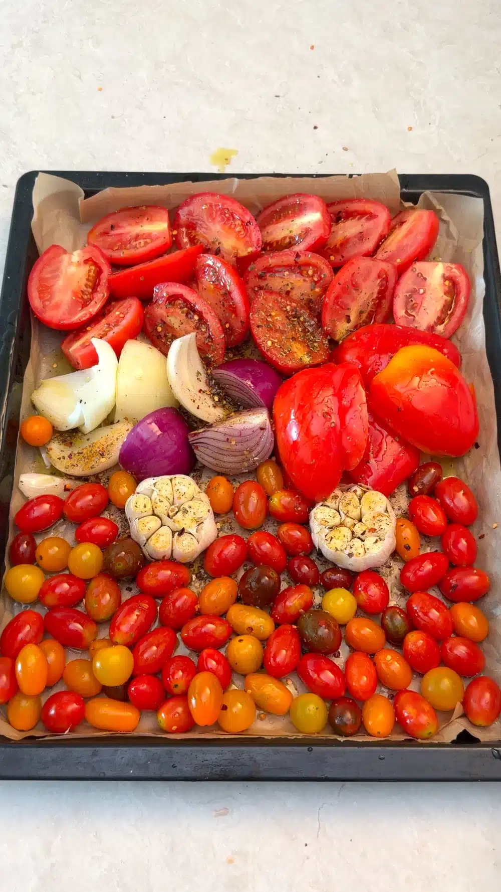 Tomatoes, red peppers, onion wedges and garlic heads seasoned on a baking tray
