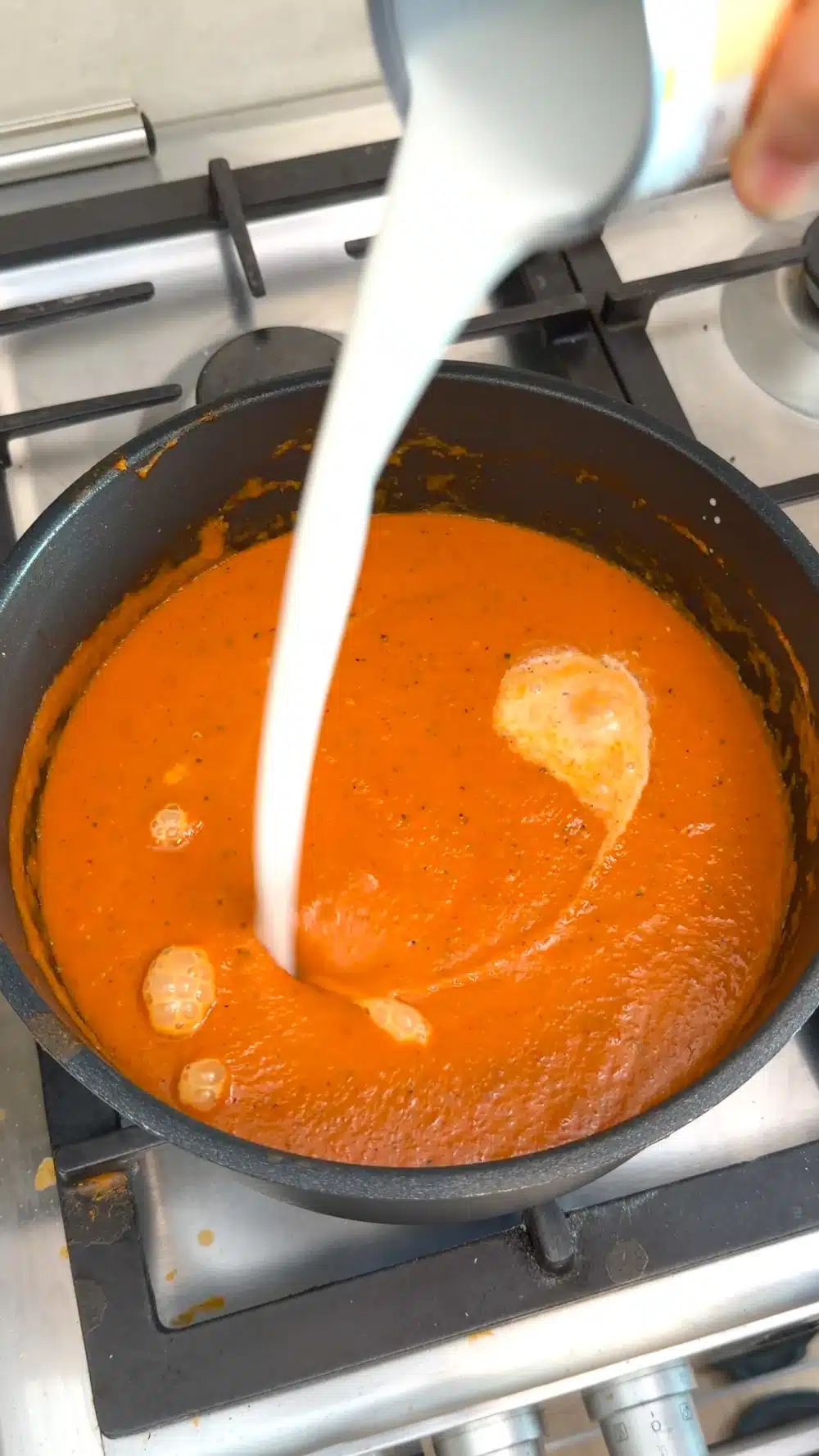 Vegan cream being poured into blended tomato and red pepper soup