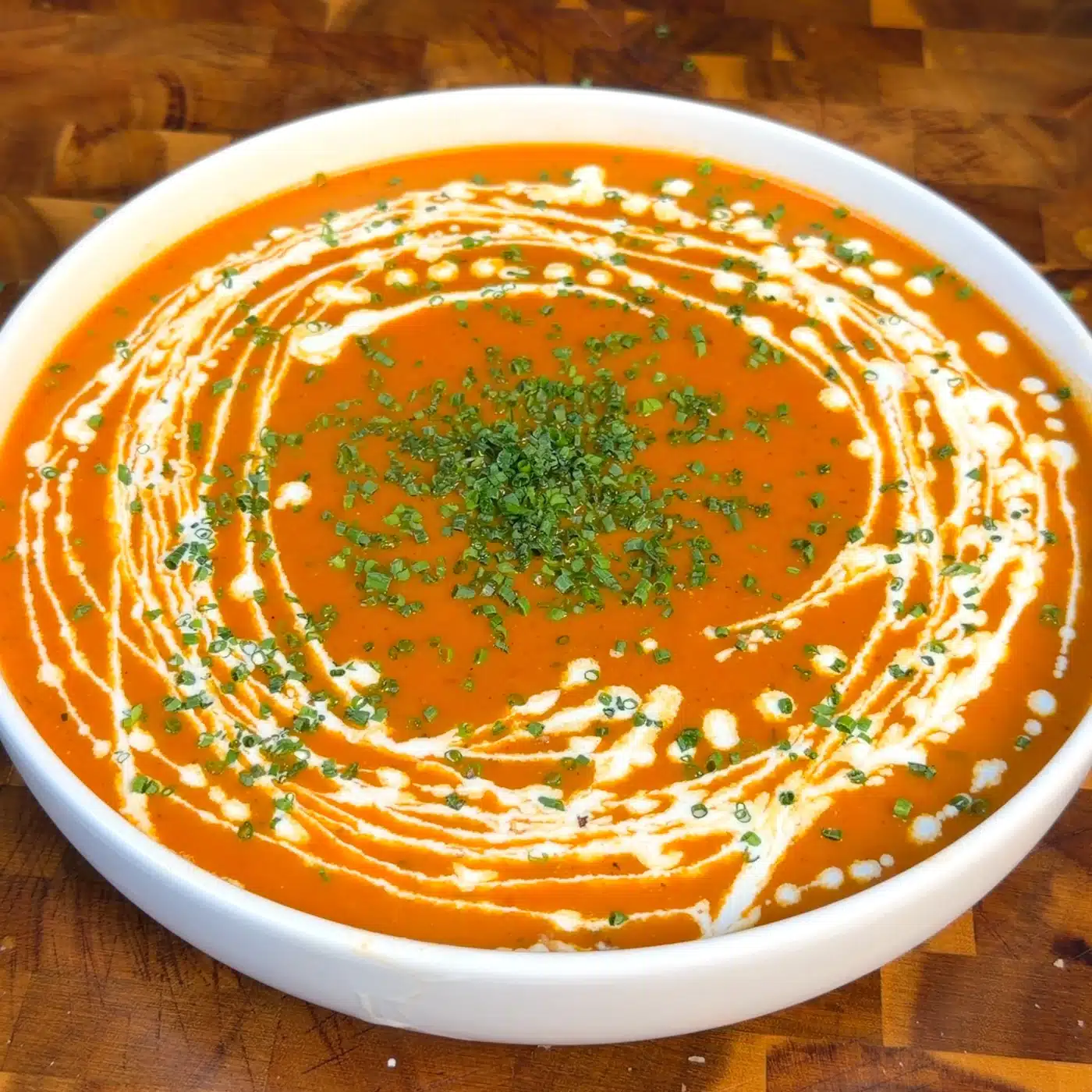 Roasted tomato and red pepper soup in a white bowl with a swirl of vegan cream and chopped herbs