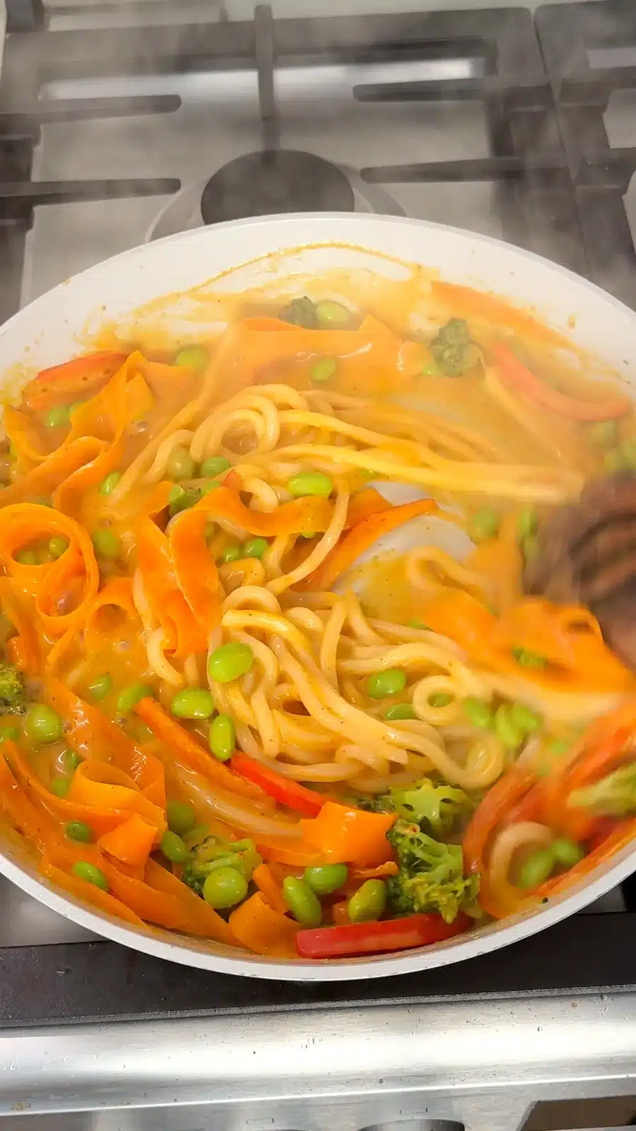 Cooked udon being tossed with vegetables and creamy curry sauce