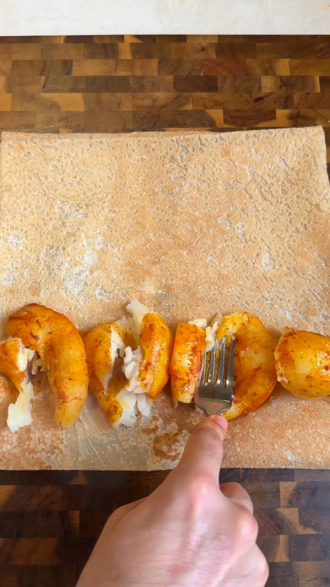 Roasted potatoes being smashed with a fork on a large lavash wrap.