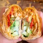 Two halves of a roasted veggie wrap with potatoes, chickpeas, peppers, cucumber and garlic yogurt sauce.