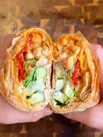 Two halves of a roasted veggie wrap with potatoes, chickpeas, peppers, cucumber and garlic yogurt sauce.